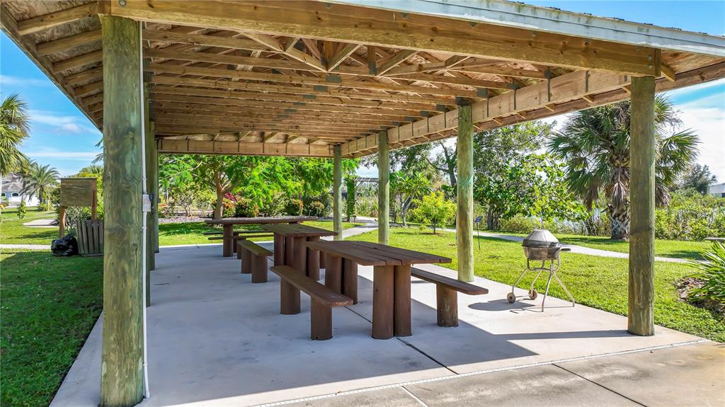 A covered outdoor pavilion with wooden picnic tables and a charcoal grill on a concrete slab — 10444 PORT EVERGLADES STREET, PORT CHARLOTTE, FL