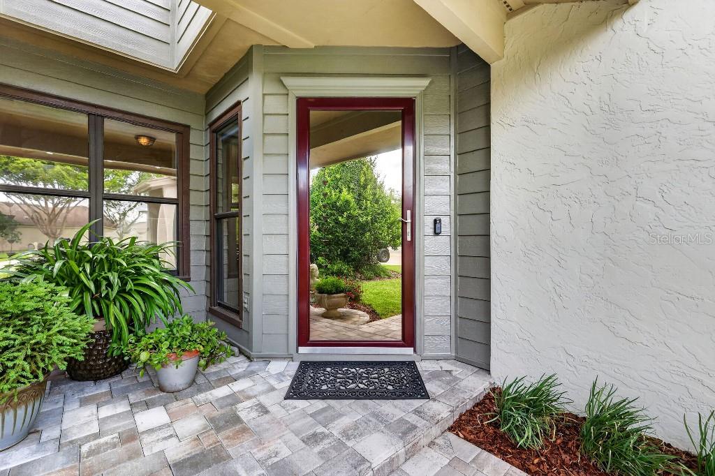 A red-framed glass storm door sits at the entrance of a home with stone pavers — 4404 NE 4TH STREET, OCALA, FL
