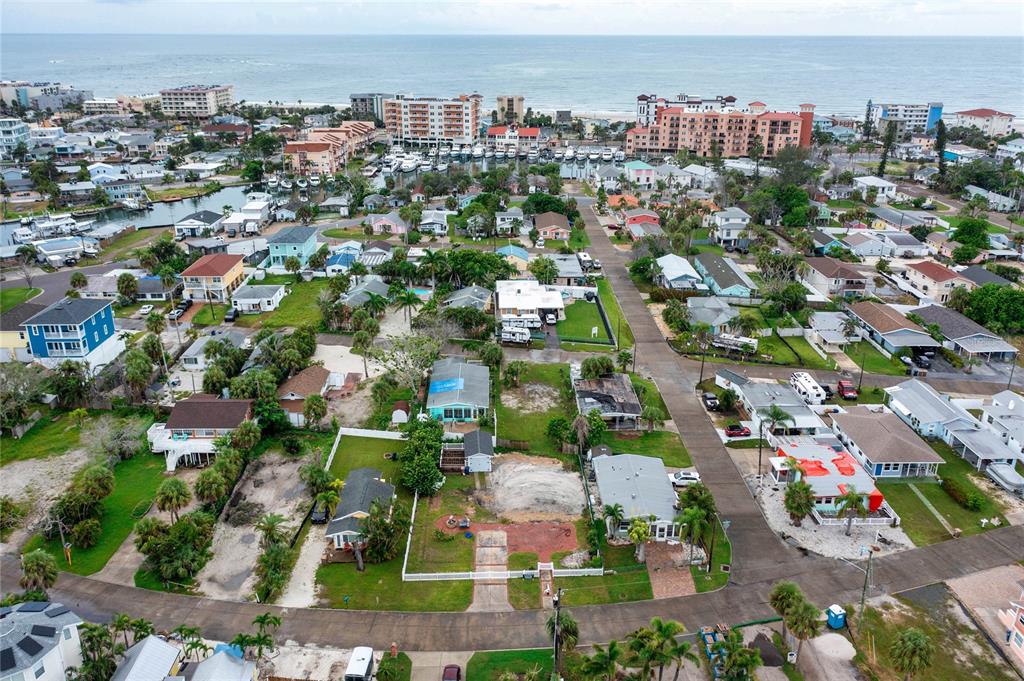 An aerial view shows a coastal neighborhood with houses, a marina, and the ocean — 13150 BOCA CIEGA AVENUE, MADEIRA BEACH, FL