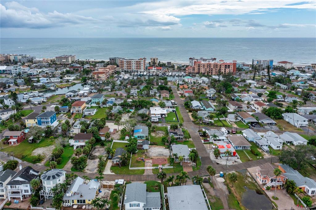 An aerial view shows a coastal neighborhood with houses, a marina, and the ocean beyond — 13150 BOCA CIEGA AVENUE, MADEIRA BEACH, FL
