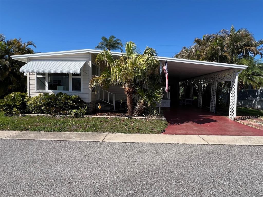 A single-story manufactured home with a white exterior, a metal awning, and a red carport — 29250 US HIGHWAY 19 N UNIT 610, CLEARWATER, FL