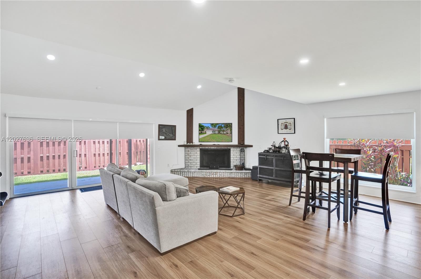A living and dining area features a brick fireplace, wood flooring, and sliding glass doors — 8946 SW 150th Ct Cir E, Miami FL 33196, MIAMI, FL