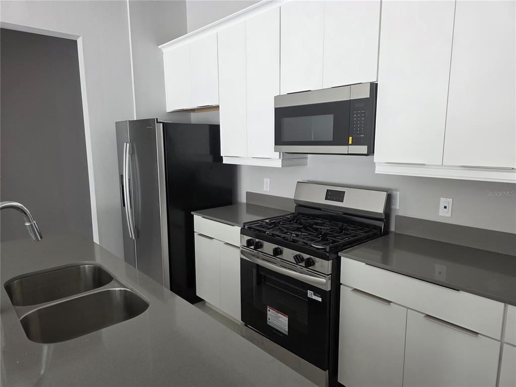 A kitchen features white cabinets, gray countertops, stainless steel appliances, and a black refrigerator — 7760 SANDY RIDGE DRIVE UNIT 112, REUNION, FL
