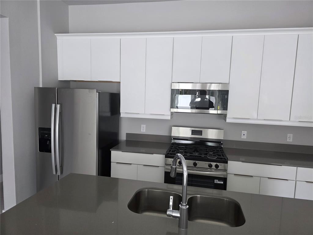 A modern kitchen features white cabinets, stainless steel appliances, and dark gray countertops — 7760 SANDY RIDGE DRIVE UNIT 112, REUNION, FL
