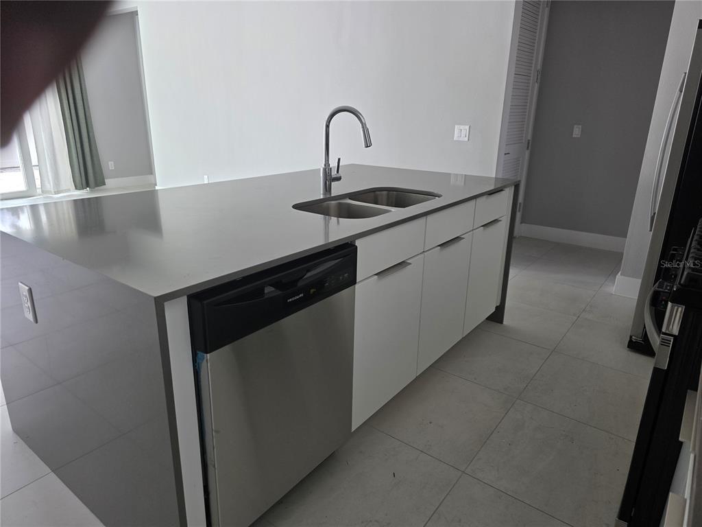 A kitchen island features a stainless steel dishwasher, a sink with a faucet, and cabinets — 7760 SANDY RIDGE DRIVE UNIT 112, REUNION, FL