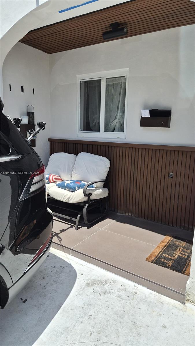 A covered patio features a white loveseat, a brown wood-slat wall, and a doormat — 7190 W 17th Ct, Hialeah FL 33014, HIALEAH, FL