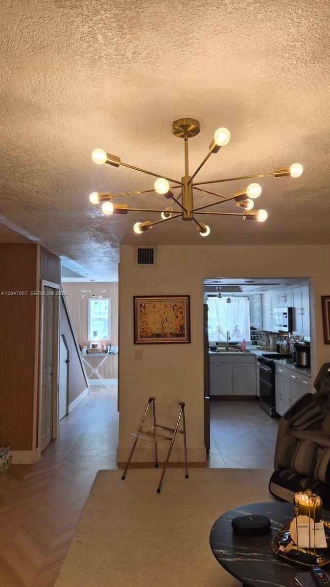 A living area features a modern gold chandelier, a hallway, and an adjacent kitchen — 7190 W 17th Ct, Hialeah FL 33014, HIALEAH, FL