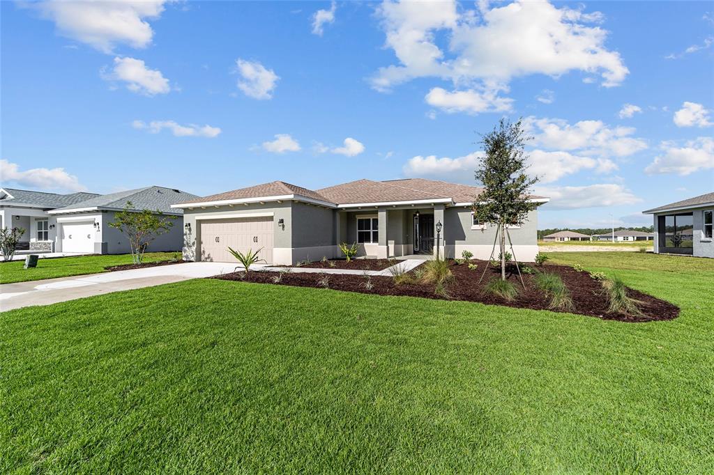 A single-story suburban house with a two-car garage, tan stucco exterior, and landscaped front yard — 10372 SW 105TH COURT, OCALA, FL