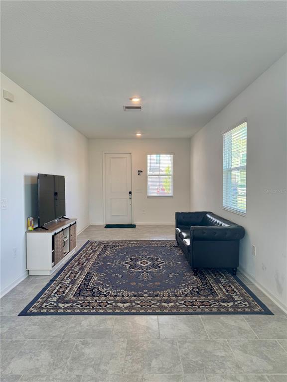 A living room features light tile flooring, a dark leather sofa, and a large area rug — 7613 STONE CREEK TRAIL, KISSIMMEE, FL