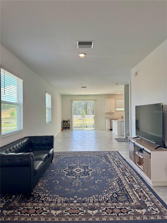 A living room features a black leather sofa, a patterned rug, and a television console — 7613 STONE CREEK TRAIL, KISSIMMEE, FL