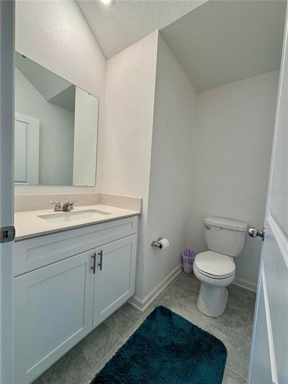 A small bathroom features a white vanity with a quartz countertop and a toilet — 7613 STONE CREEK TRAIL, KISSIMMEE, FL