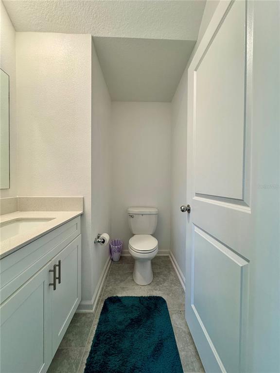 A small bathroom features a white vanity, a toilet, and gray tile flooring — 7613 STONE CREEK TRAIL, KISSIMMEE, FL