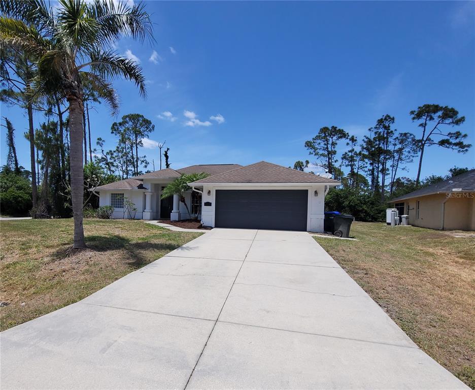A single-story house with a white exterior, a dark garage door, and a concrete driveway — 1402 JAKWAY ROAD, NORTH PORT, FL