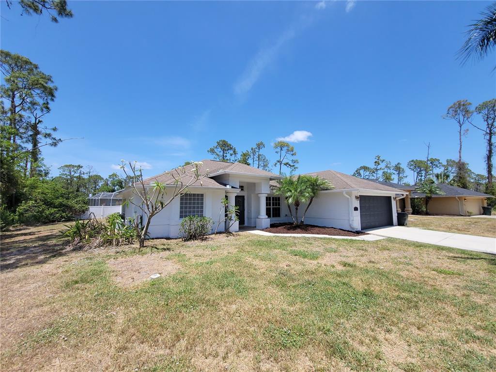 A single-story white house with a dark garage door and a front yard — 1402 JAKWAY ROAD, NORTH PORT, FL