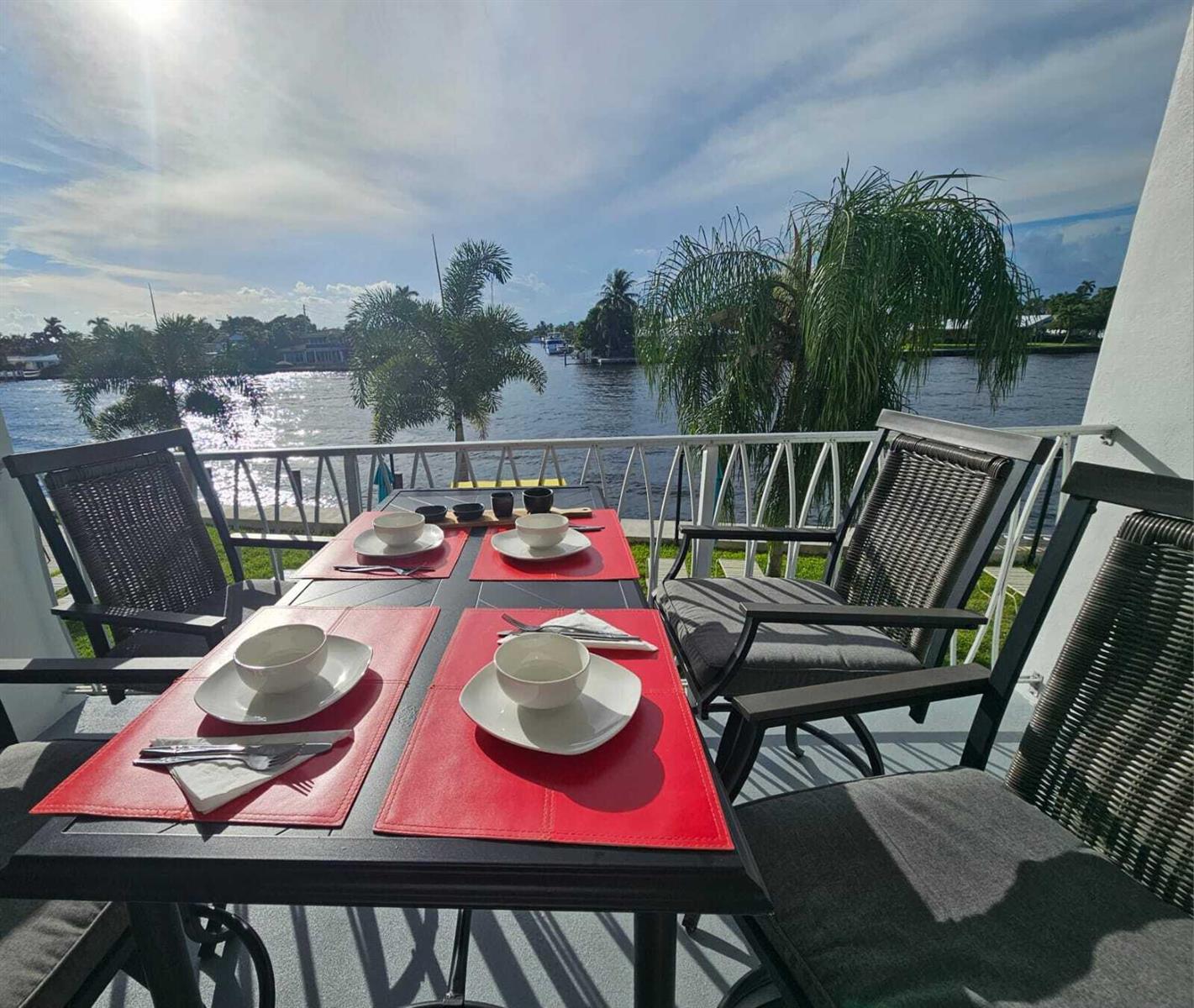 A patio dining set overlooks a canal with palm trees under a sunny sky — 505 N Riverside Drive # 12a, Pompano Beach FL 33062, POMPANO BEACH, FL