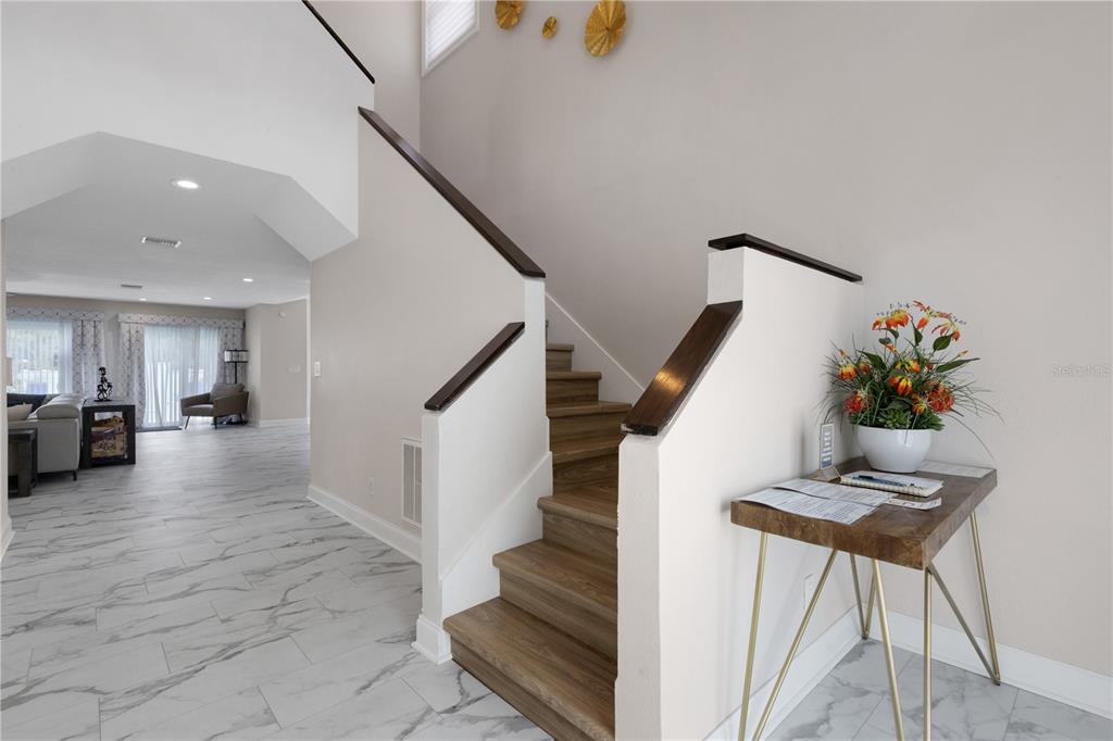 An entryway features a wooden staircase, marble-look tile flooring, and a small console table — 4124 HARBOR CIRCLE S, LARGO, FL