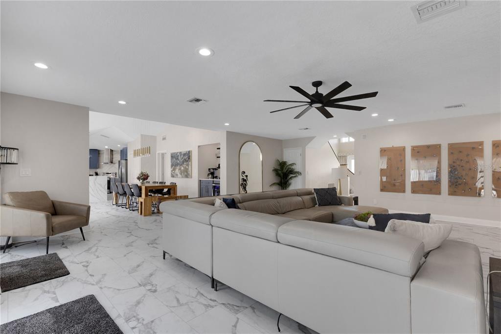 A spacious living room features a large sectional sofa, marble-look tile flooring, and a ceiling fan — 4124 HARBOR CIRCLE S, LARGO, FL