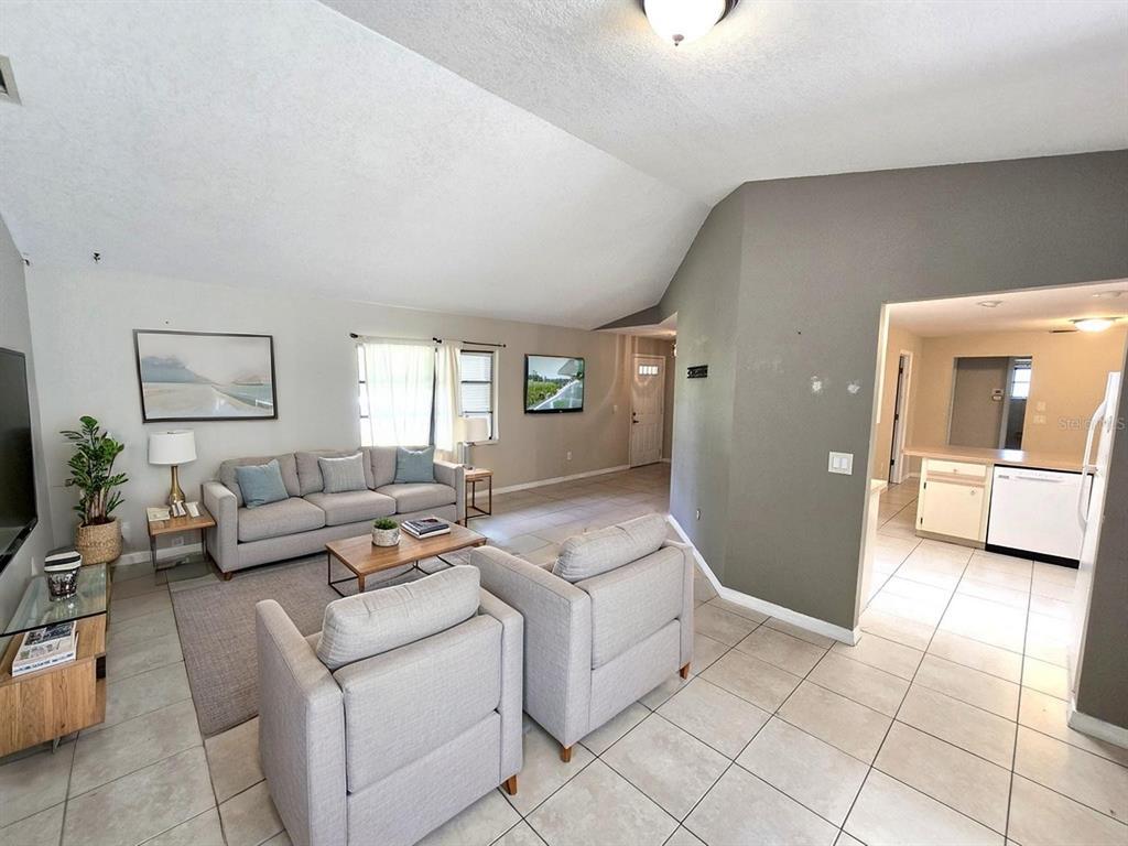 A living room with light tile floors, gray furniture, and an open view to the kitchen — 279 KINDRED BOULEVARD, PORT CHARLOTTE, FL