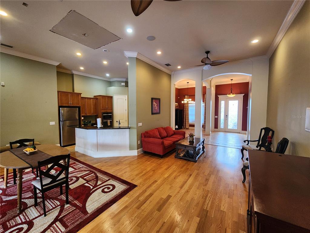 An open-concept living and dining area features hardwood floors, a red sofa, and kitchen cabinetry — 2832 VINTAGE VIEW LOOP, LAKELAND, FL
