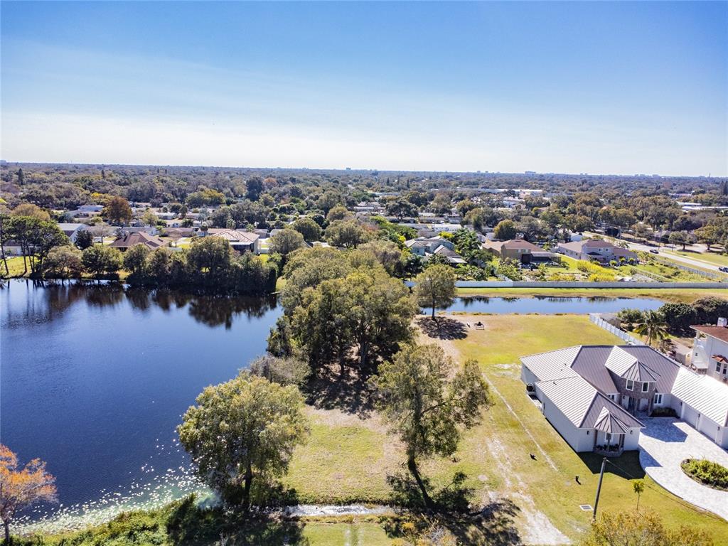 An aerial view shows a house with a metal roof next to a large lake — 5750 60TH AVENUE N, ST PETERSBURG, FL
