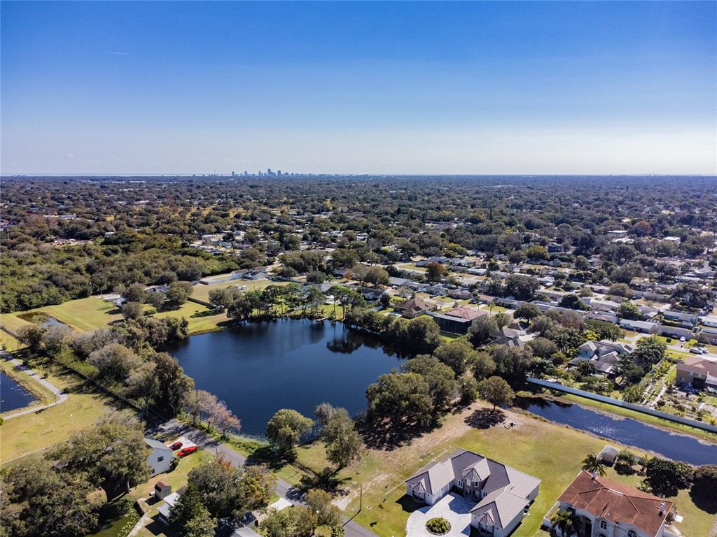 An aerial view shows a suburban neighborhood with a lake and a distant city skyline — 5750 60TH AVENUE N, ST PETERSBURG, FL