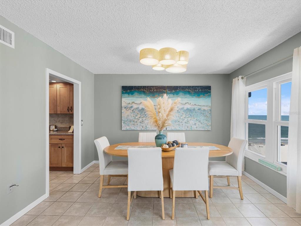 A dining room features a wooden table, white chairs, a coastal painting, and ocean views — 17400 GULF BOULEVARD UNIT J7, ST PETERSBURG, FL