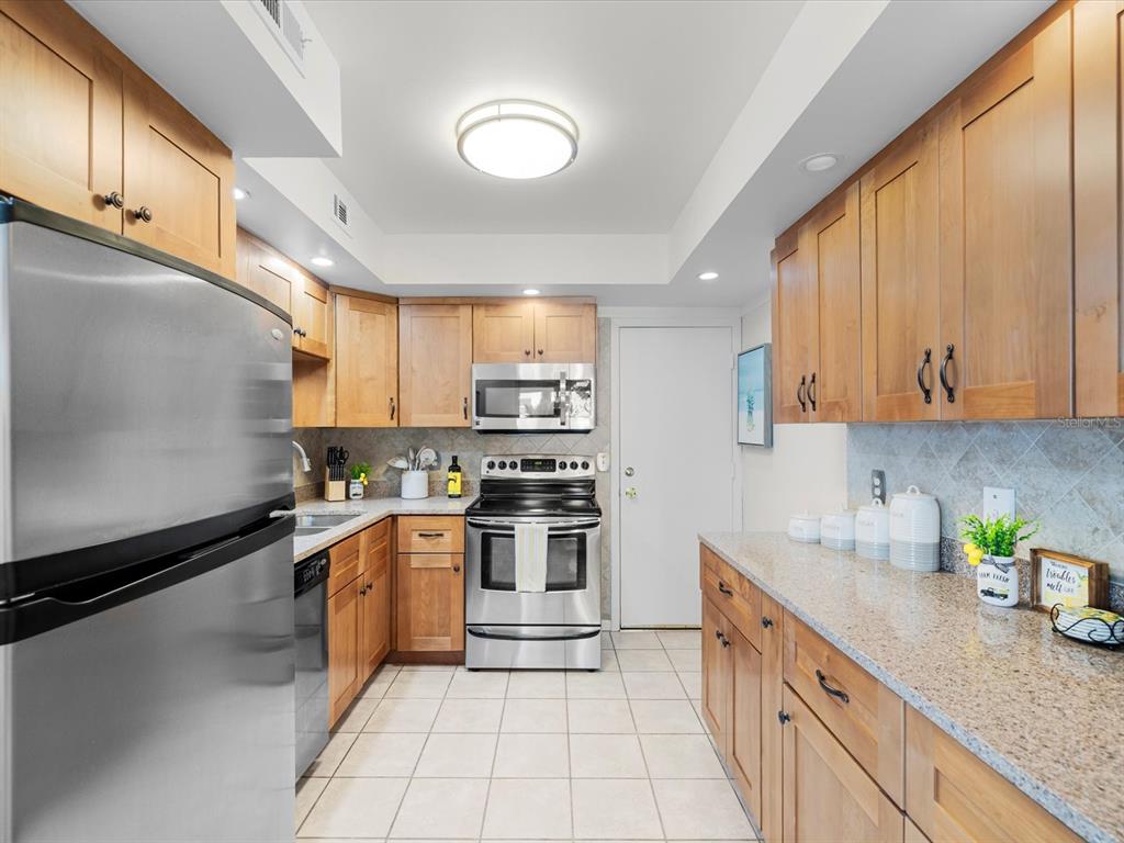 A kitchen features stainless steel appliances, light wood cabinets, granite countertops, and tiled flooring — 17400 GULF BOULEVARD UNIT J7, ST PETERSBURG, FL