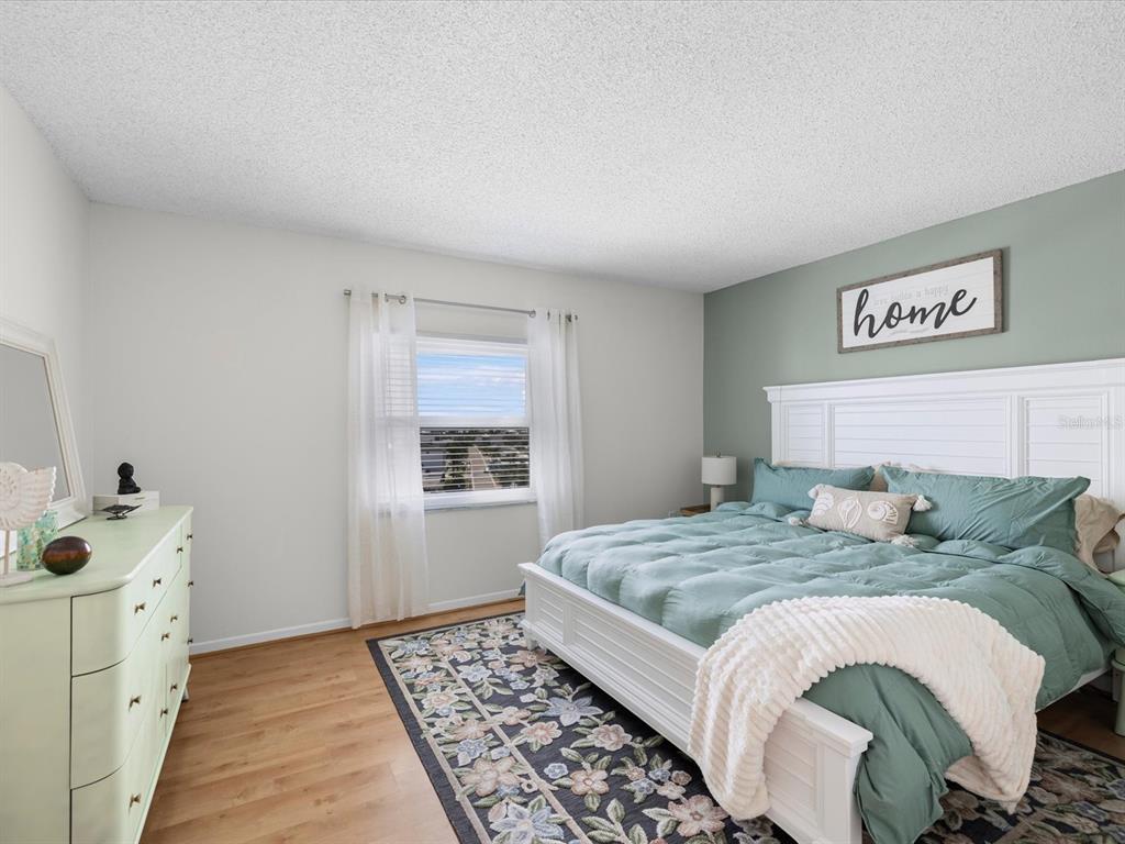 A bedroom features a white bed frame, green bedding, a floral rug, and a green dresser — 17400 GULF BOULEVARD UNIT J7, ST PETERSBURG, FL