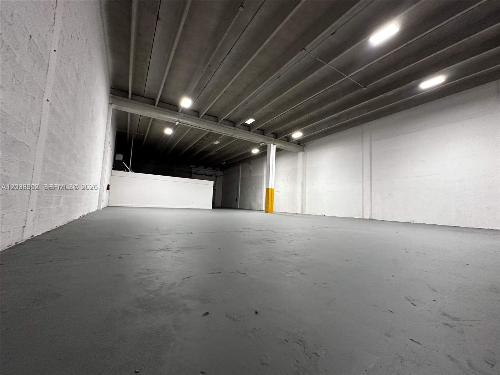 An empty industrial warehouse space features a gray concrete floor and white painted walls — MIAMI, FL