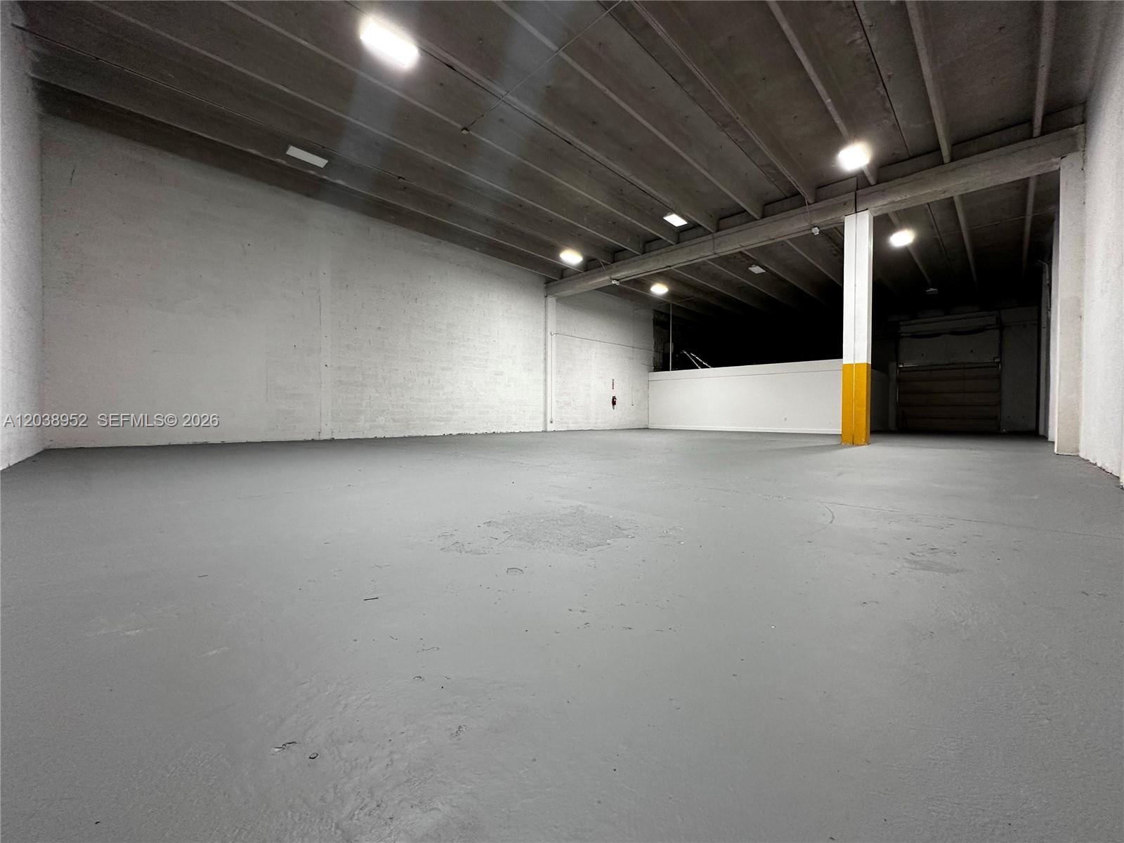 An empty warehouse space features white concrete walls, a gray floor, and overhead lighting — MIAMI, FL