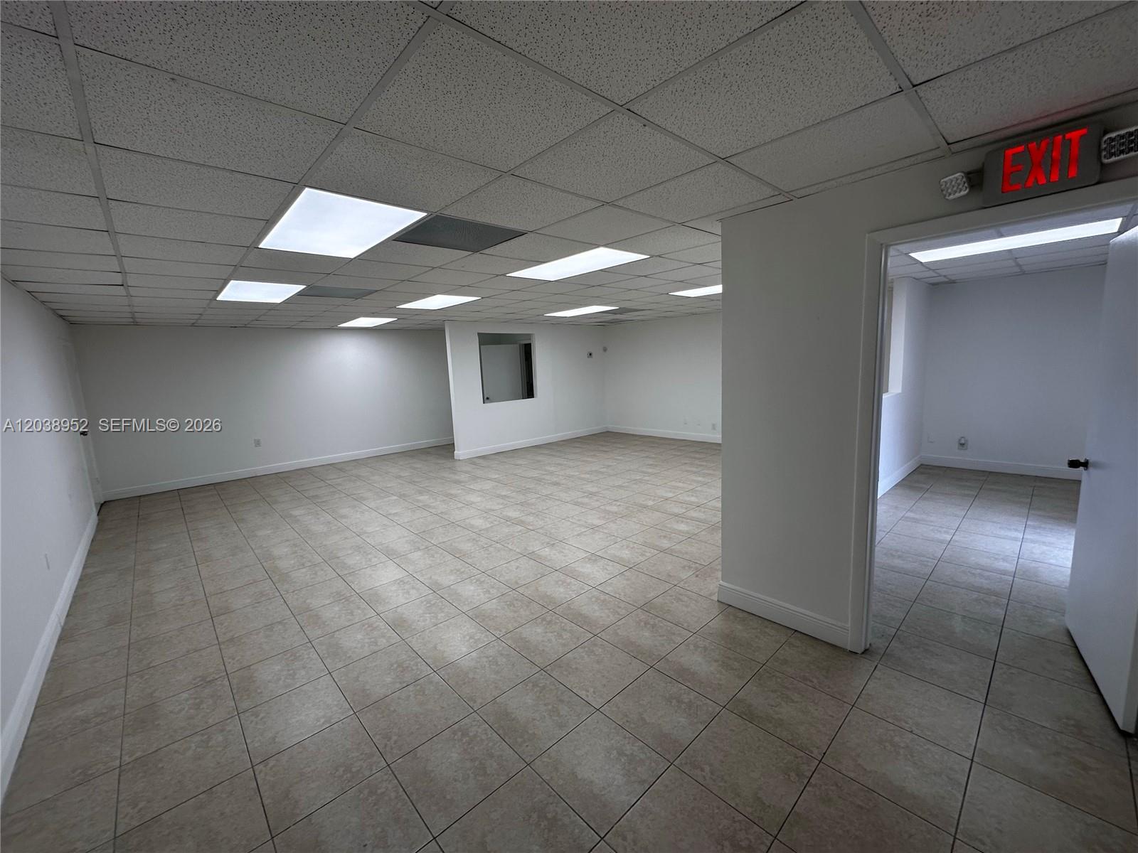 An empty office space features a drop ceiling, tiled floors, and an illuminated exit sign — MIAMI, FL