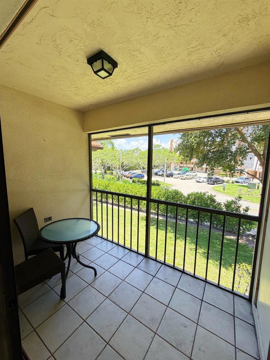 A screened-in balcony with tiled flooring, a small table, two chairs, and a parking view — 351 Club Circle # 208, Boca Raton FL 33487, BOCA RATON, FL