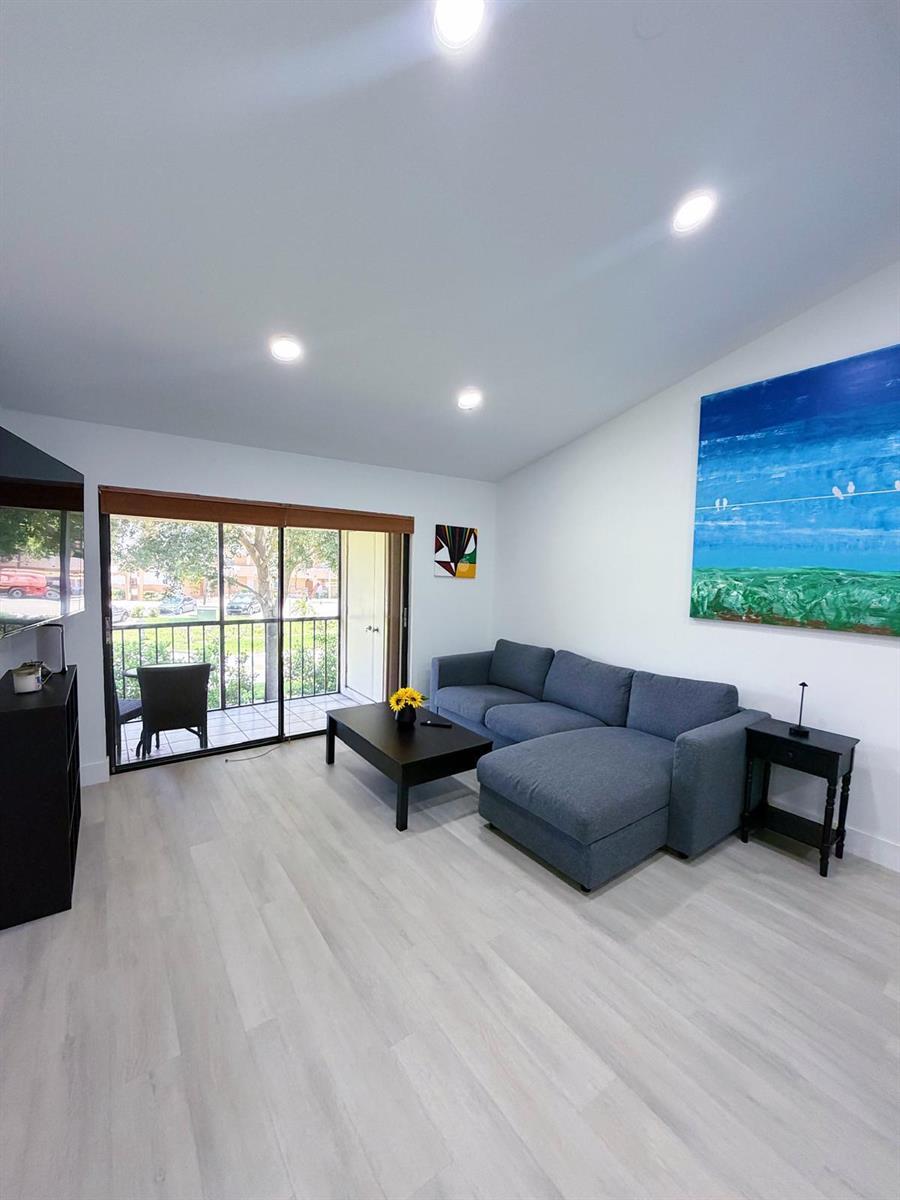 A living room features a blue sectional sofa, a coffee table, and a sliding glass door — 351 Club Circle # 208, Boca Raton FL 33487, BOCA RATON, FL