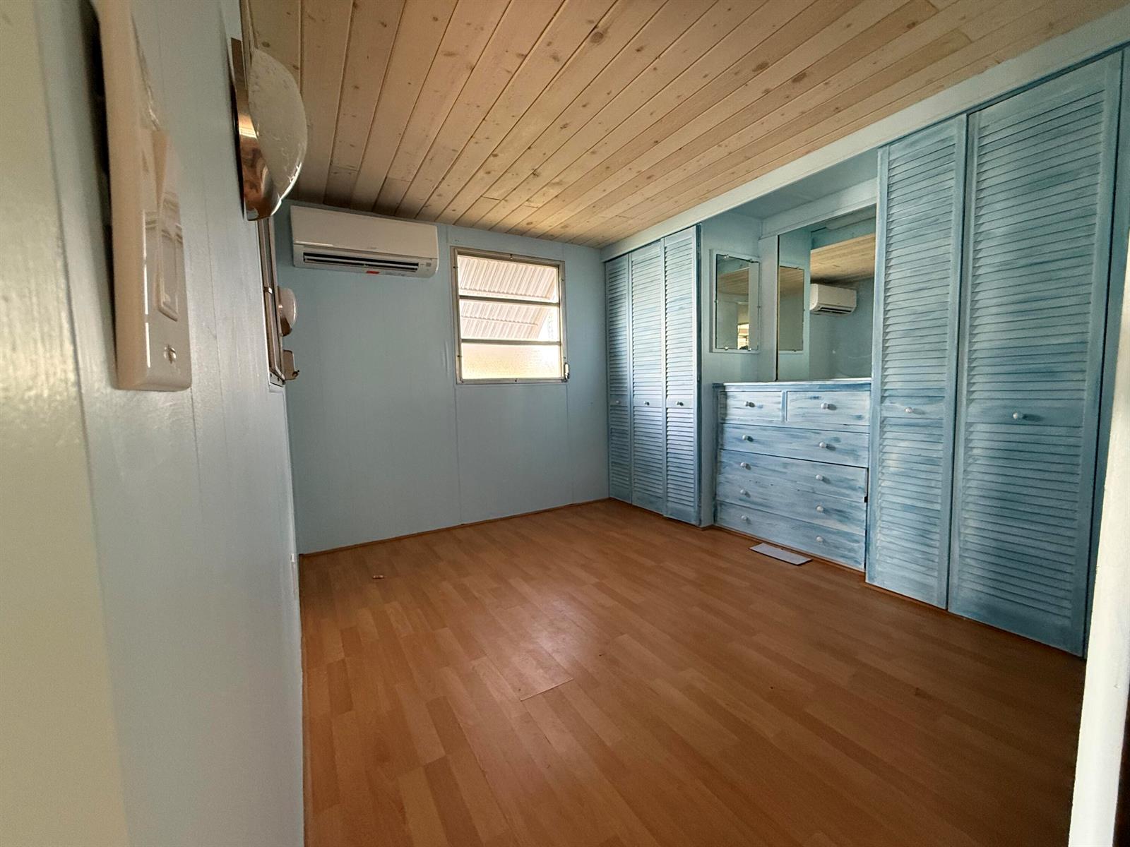 An empty bedroom features light blue walls, wood-paneled ceilings, laminate flooring, and built-in louvered closets — 209 Eagle Drive E, Briny Breezes FL 33435, BRINY BREEZES, FL