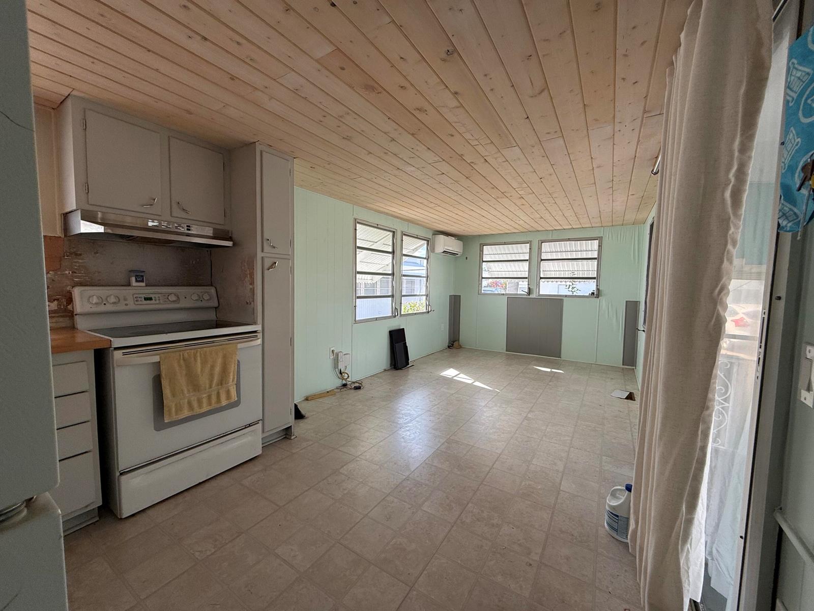 A kitchen and living area with light green walls, wood-paneled ceiling, and tile flooring — 209 Eagle Drive E, Briny Breezes FL 33435, BRINY BREEZES, FL