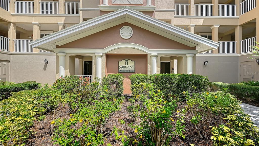 The exterior of a multi-story apartment building features a covered entrance with a central sign — 5222 MANORWOOD DRIVE UNIT 4A, SARASOTA, FL