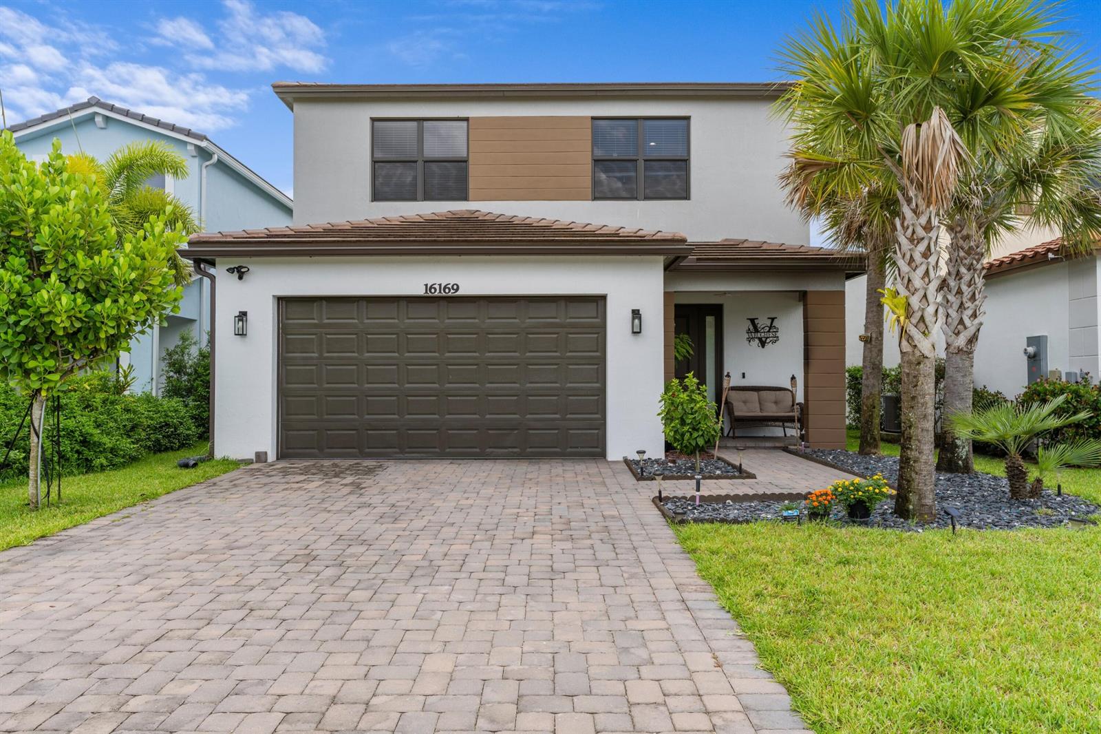 A two-story house features a paved driveway, a brown garage door, and palm trees — 16169 Sea Turtle Place, Westlake FL 33470, WESTLAKE, FL