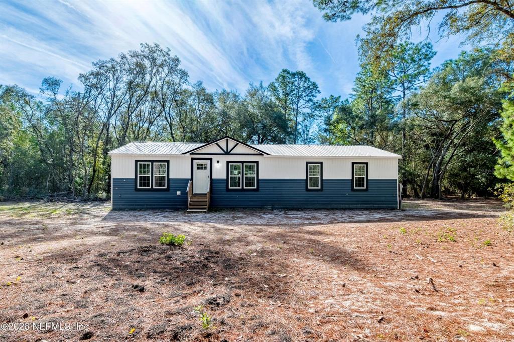 A single-story house with white and blue siding stands in a wooded lot — 7577 HOT SPRINGS COURT, KEYSTONE HEIGHTS, FL