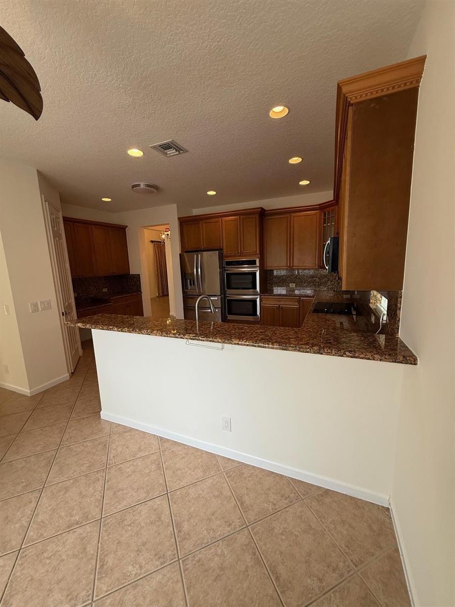 A kitchen features wood cabinets, granite countertops, stainless steel appliances, and tile flooring — 12039 Oakvista Drive, Boynton Beach FL 33437, BOYNTON BEACH, FL