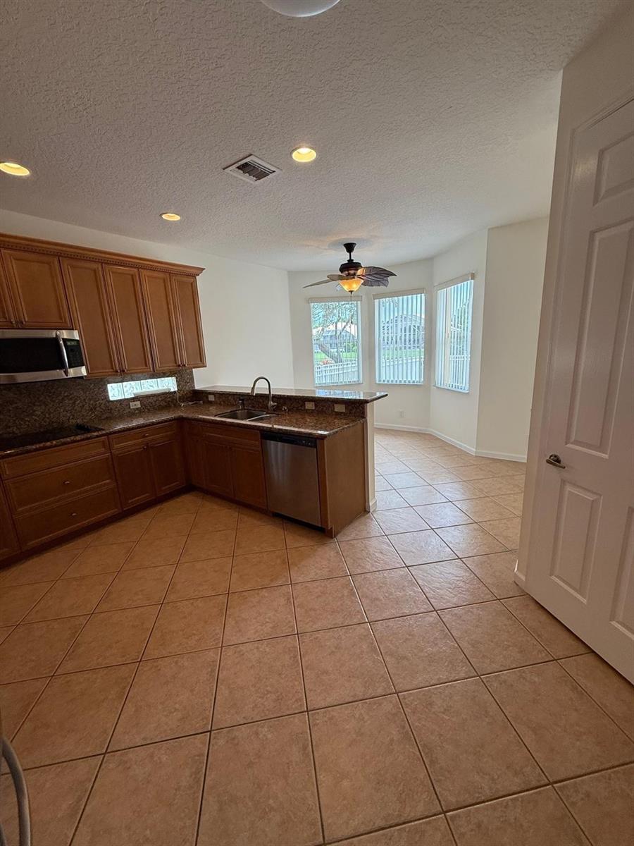 A kitchen with wood cabinets, granite countertops, and tile flooring opens to a dining area — 12039 Oakvista Drive, Boynton Beach FL 33437, BOYNTON BEACH, FL