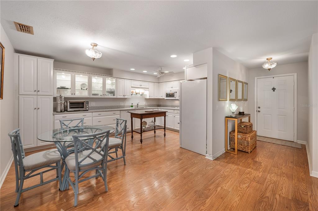 A kitchen with white cabinetry, a glass dining table, and wood flooring near an entryway — 26 BUCK CIRCLE, HAINES CITY, FL