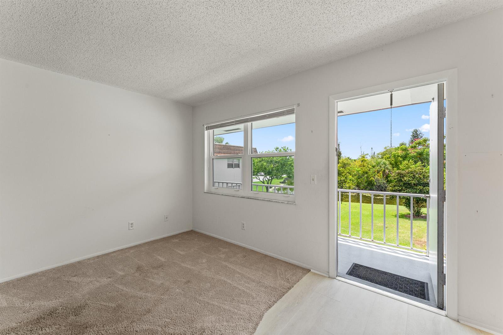 An empty room with beige carpet, white walls, a window, and a door to a balcony — 1225 NW 21st Street # 710, Stuart FL 34994, STUART, FL