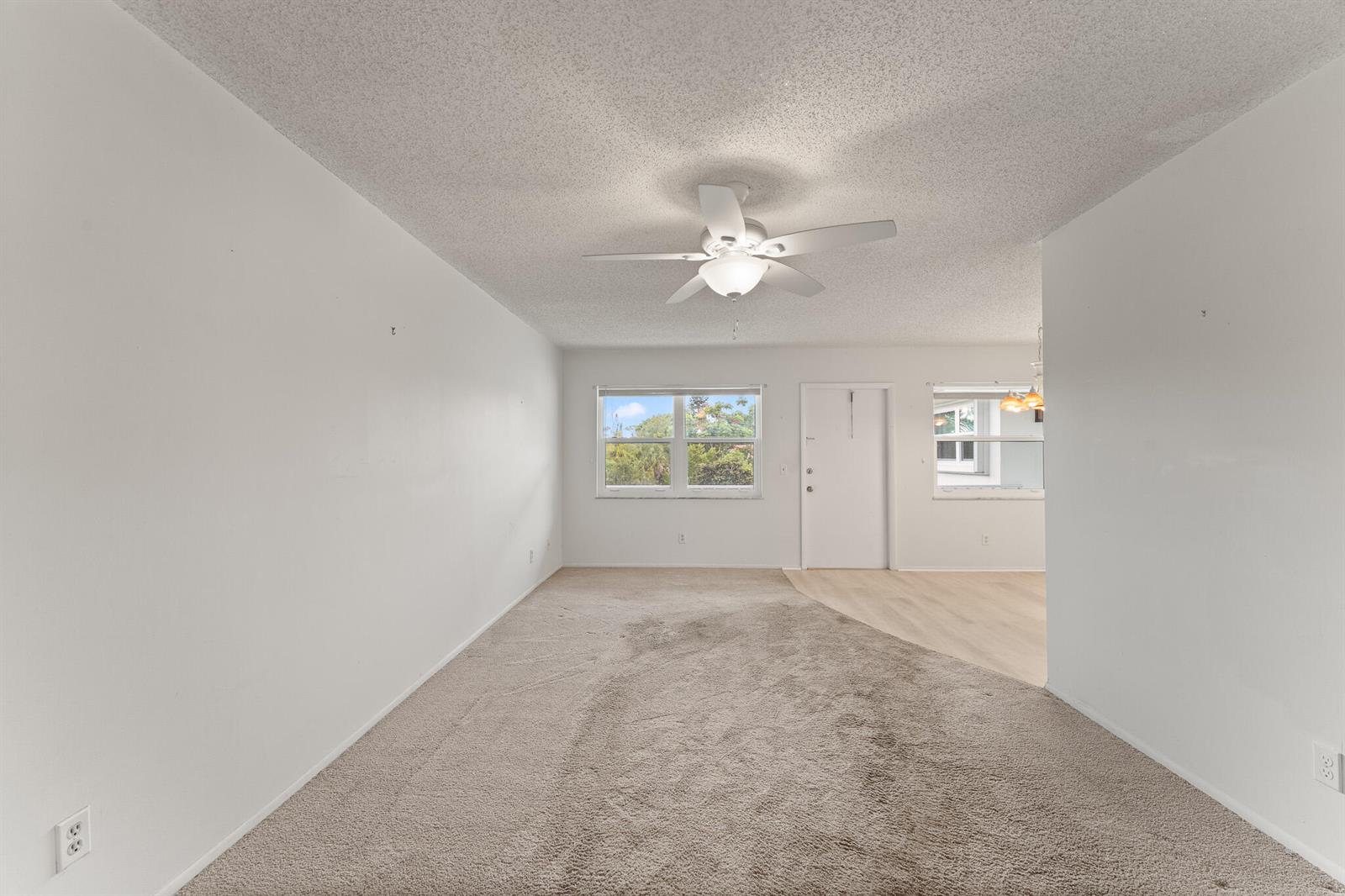 An empty living room features beige carpeting, white walls, a ceiling fan, and a window — 1225 NW 21st Street # 710, Stuart FL 34994, STUART, FL
