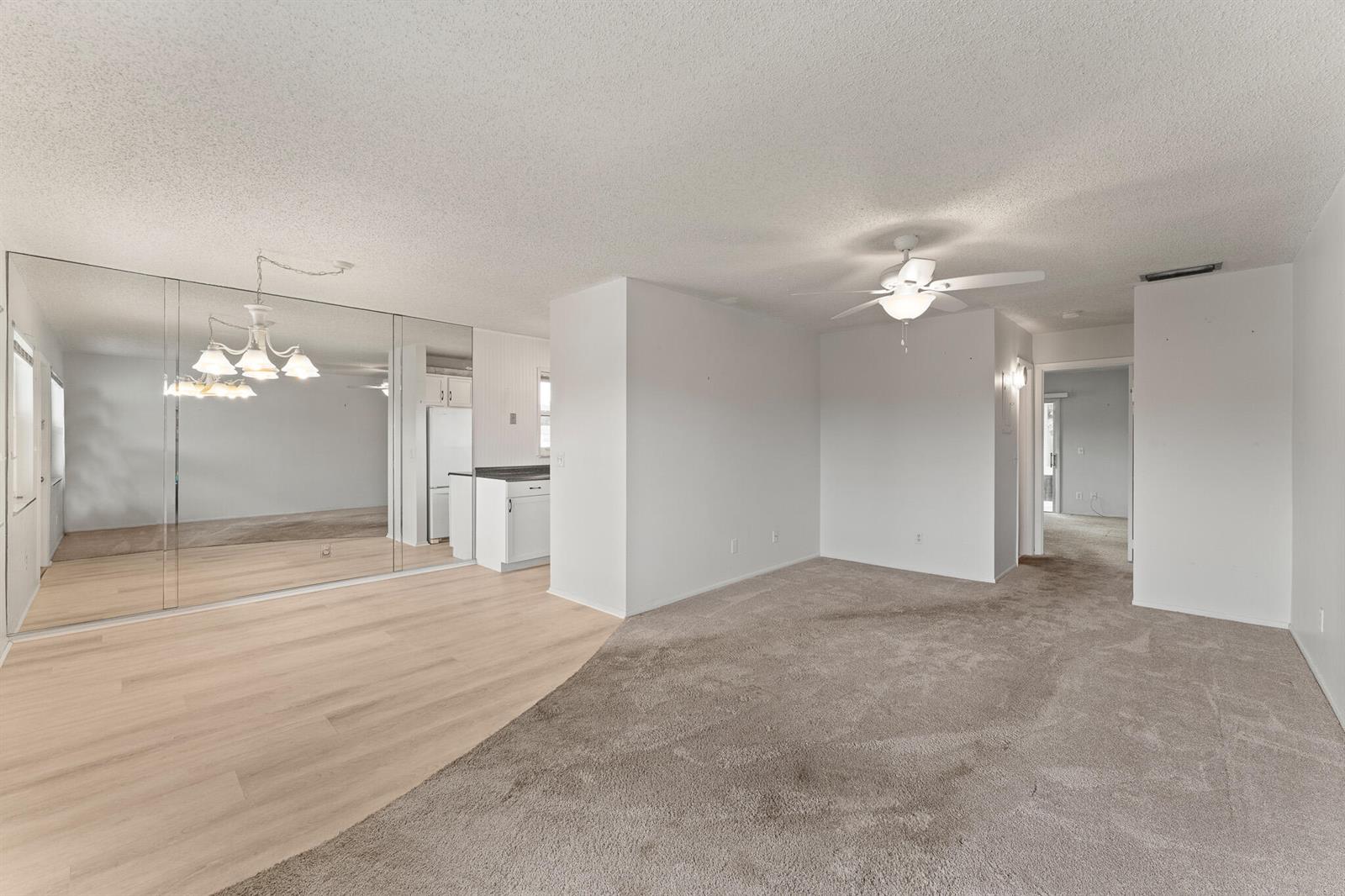 A living room with carpet, wood-look flooring, mirrored walls, and a ceiling fan — 1225 NW 21st Street # 710, Stuart FL 34994, STUART, FL