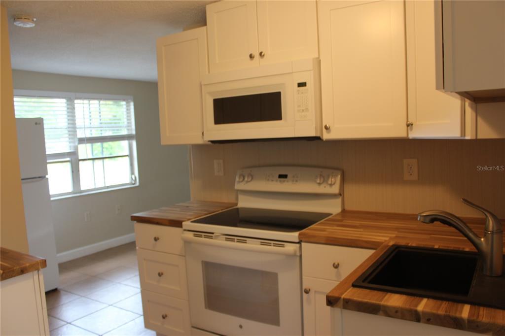 A kitchen features white cabinets, a microwave, a white stove, and wood-look countertops — 4424 TERRY LOOP, NEW PORT RICHEY, FL