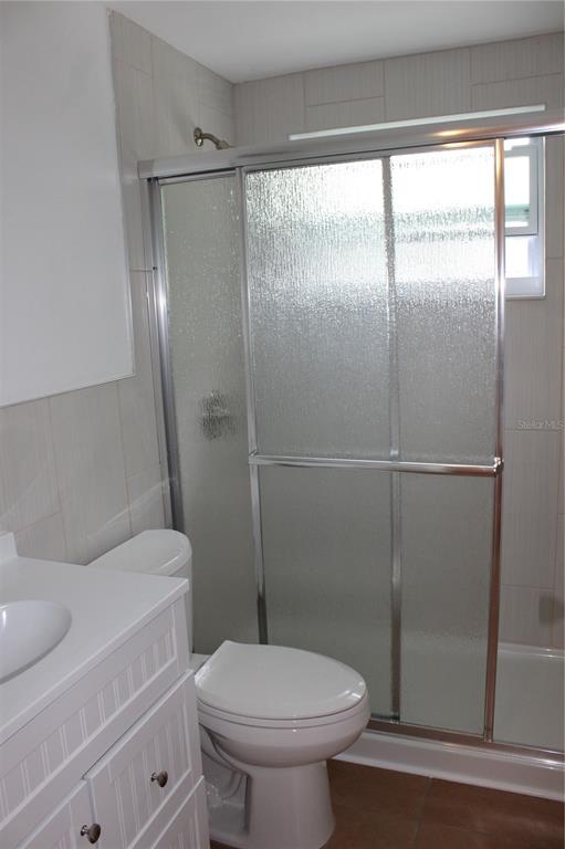 A bathroom features a white vanity, a toilet, and a walk-in shower with glass doors — 4424 TERRY LOOP, NEW PORT RICHEY, FL