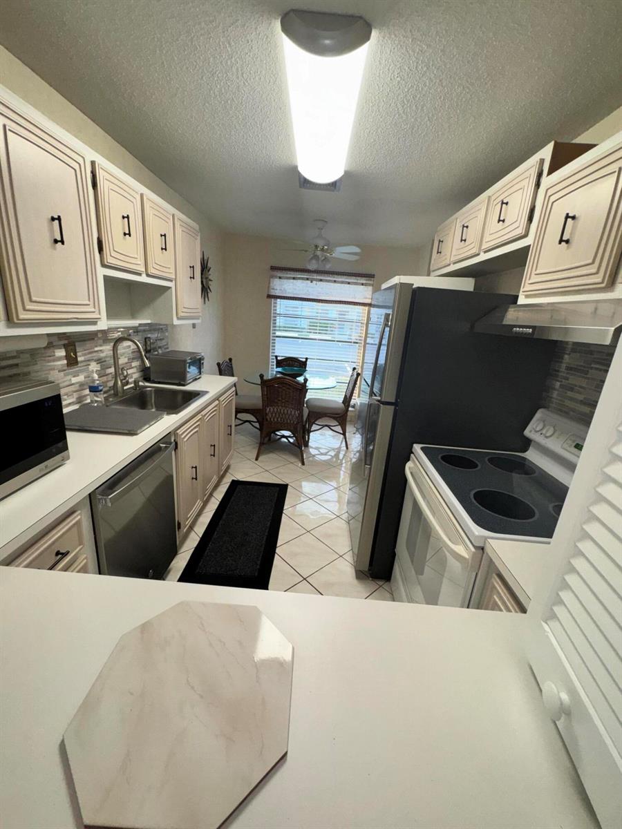 A galley kitchen features light-colored cabinets, stainless steel appliances, and a small dining area — 13731 Flora Place # C, Delray Beach FL 33484, DELRAY BEACH, FL
