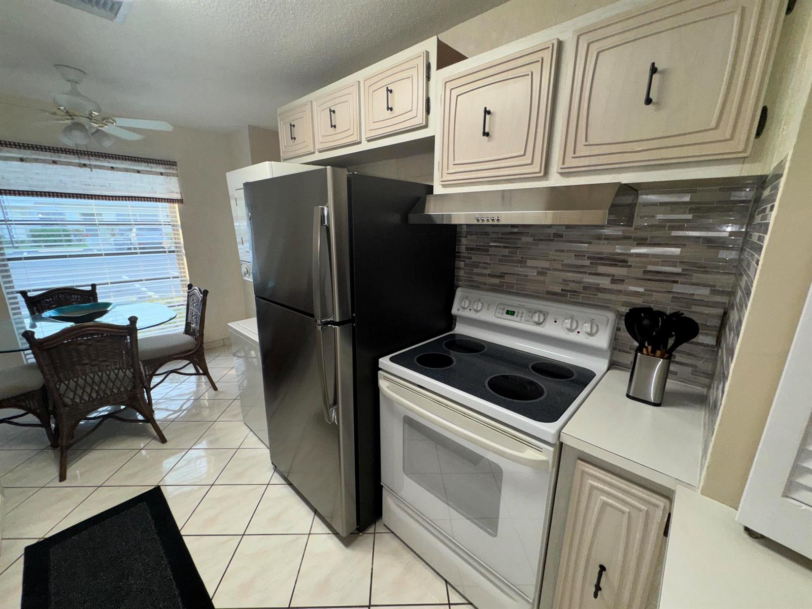 A kitchen features a black refrigerator, white stove, light cabinets, and a dining area nearby — 13731 Flora Place # C, Delray Beach FL 33484, DELRAY BEACH, FL