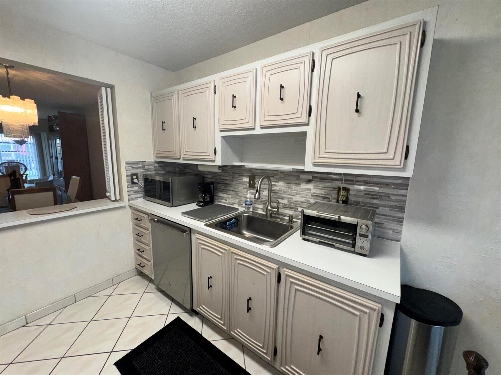 A kitchen features light-colored cabinets, a stainless steel sink, and a tiled backsplash — 13731 Flora Place # C, Delray Beach FL 33484, DELRAY BEACH, FL