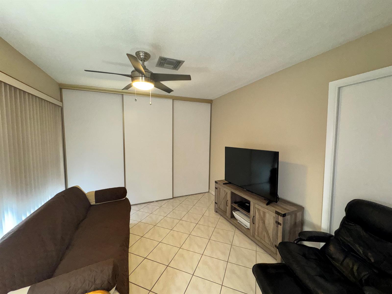 A living room features a brown sofa, a television on a wooden stand, and tile flooring — 13731 Flora Place # C, Delray Beach FL 33484, DELRAY BEACH, FL